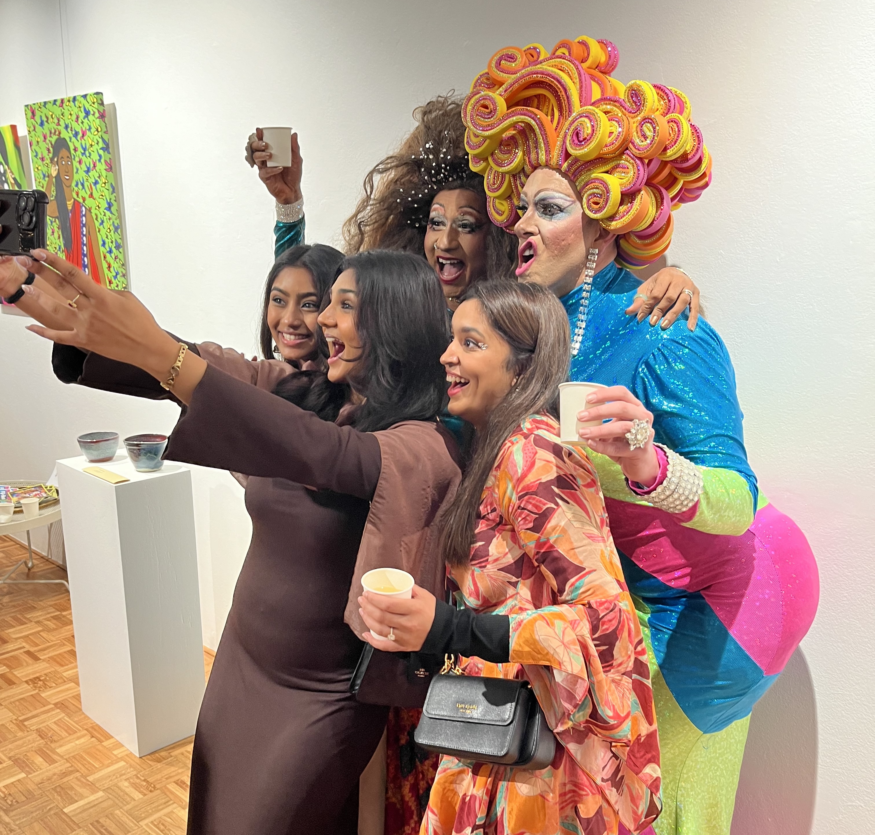 Photo of group of young women posing with drag queens at the Chrissie Cotter Gallery, one woman holds her phone and they all pose excitedly for the photo